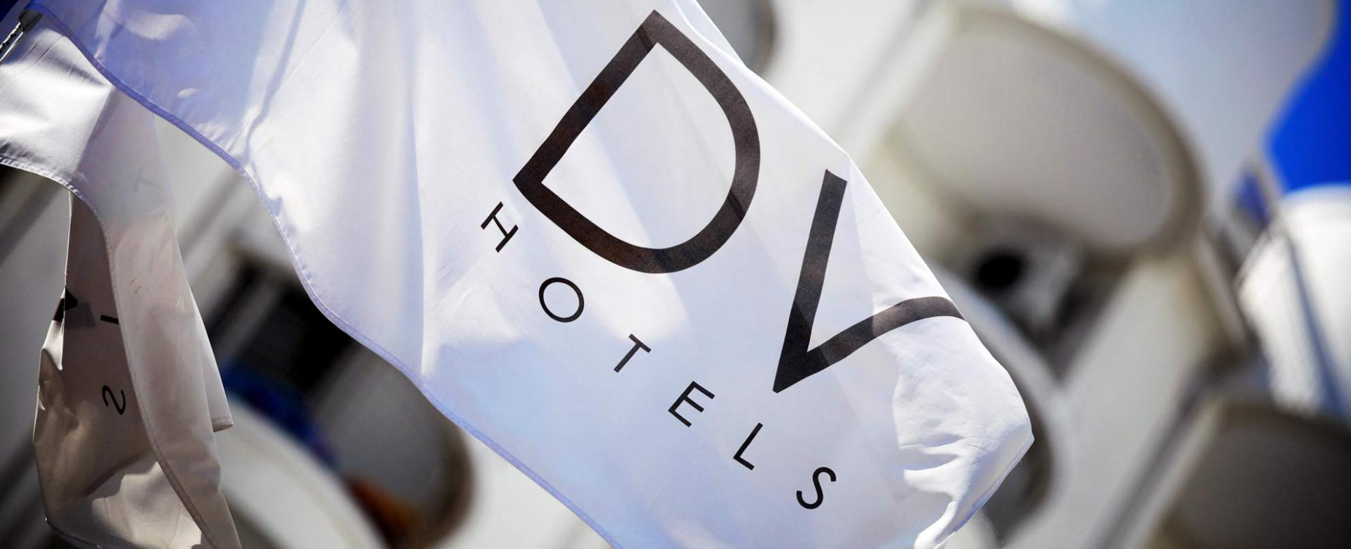 Bandiera bianca ondeggia con scritta DV Hotels, atmosfera elegante e moderna.