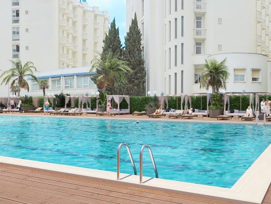 Outdoor pool surrounded by loungers and palm trees.