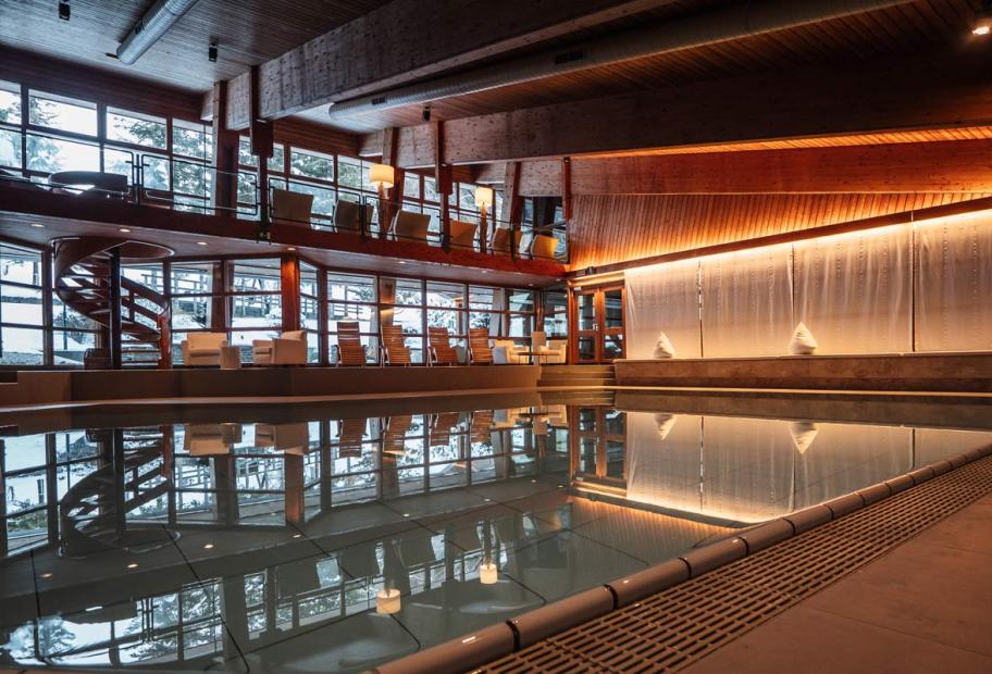 Piscina interna elegante, legno caldo e luci soffuse, atmosfera rilassante e lussuosa.