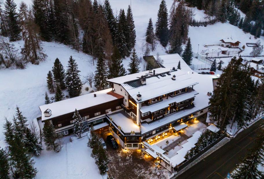 Hotel innevato tra abeti, atmosfera calda e accogliente di montagna.